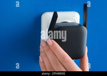 Femme branchant un répéteur WiFi noir dans la prise électrique murale bleue Banque D'Images