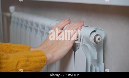 Les mains des femmes essaient de rester au chaud sur un radiateur en aluminium. Une femme se réchauffe près d'un radiateur en hiver pendant la crise énergétique en Europe Banque D'Images