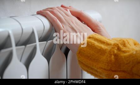 Les mains des femmes essaient de rester au chaud sur un radiateur en aluminium. Une femme se réchauffe près d'un radiateur en hiver pendant la crise énergétique en Europe Banque D'Images