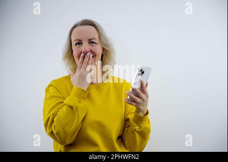 Peur drôle jeune femme caucasienne portant un T-shirt blanc sur fond blanc tenant le téléphone et les ongles de piqûres. Photo de haute qualité Banque D'Images