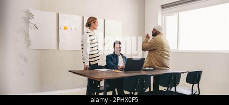 Groupe de divers hommes d'affaires ayant une discussion tout en travaillant ensemble dans un bureau créatif. Trois collègues d'affaires partagent leurs idées dans un W moderne Banque D'Images