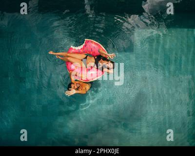 Vue aérienne du couple en vacances dans la piscine du complexe avec vue sur la caméra. Femme allongé sur un anneau gonflable et homme dans l'eau à côté de son agitant à la caméra Banque D'Images