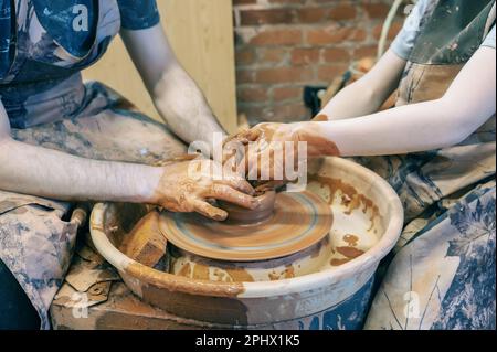 potter enseigne l'enfant. Un artisan est assis sur un banc avec une roue de potier et fait un pot en argile. Artisanat national. Gros plan des mains. Banque D'Images