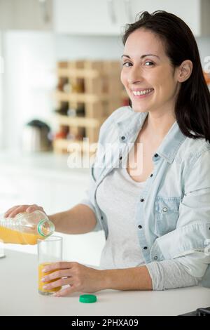 femme à la maison versant un verre de jus d'orange Banque D'Images