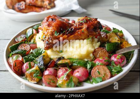 Légumes rôtis avec des pilons de poulet au barbecue et une purée de pommes de terre sur une assiette Banque D'Images