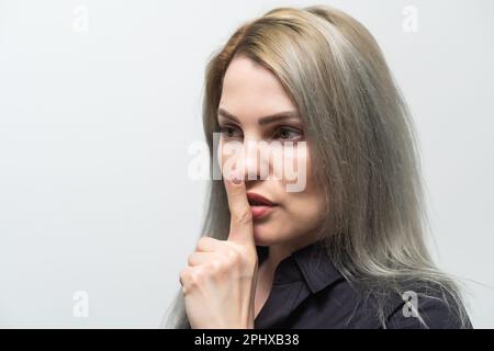 Belle jeune femme caucasienne isolée sur fond gris studio tenir le doigt sur les lèvres demander être silencieux, millénaire regarder la caméra dire Banque D'Images