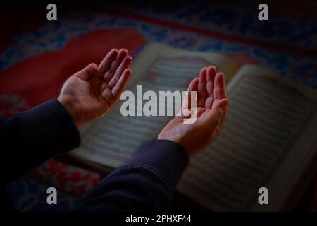 Photo islamique. Prier l'homme musulman avec les mains levées. Le Saint Coran en arrière-plan. Ramadan ou photo de concept islamique. Mise au point sélective. Banque D'Images