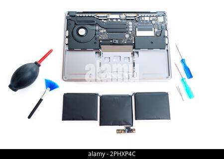 Batterie d'ordinateur portable démontée et gonflée extraite, avec tournevis, brucelles, brosse et souffleur d'air pour nettoyer la poussière du comnon Banque D'Images