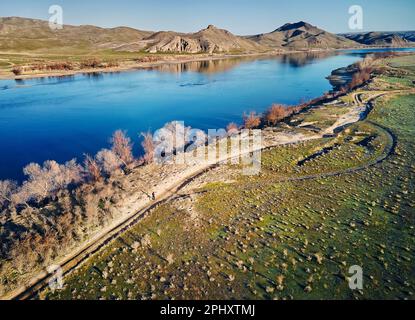 Vue aérienne par drone d'un homme sportif qui coule sur une route de campagne poussiéreuse près de la rivière et des collines au coucher du soleil. Sentier qui fonctionne à la steppe près de la rivière SG au sud Banque D'Images