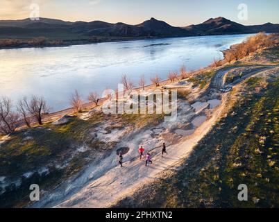 Vue aérienne par drone d'un homme sportif qui coule sur une route de campagne poussiéreuse près de la rivière et des collines au coucher du soleil. Sentier qui fonctionne à la steppe près de la rivière SG au sud Banque D'Images