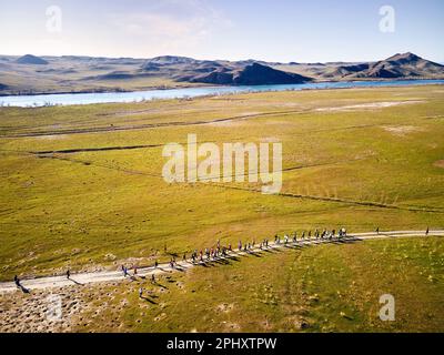 Vue aérienne par drone de la foule les gens qui se livrent à la compétition sur une route de campagne poussiéreuse près de la rivière et des collines au coucher du soleil. Sentier qui fonctionne à la steppe près de la riv de SG Banque D'Images