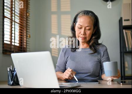 Femme d'affaires asiatique professionnelle et concentrée utilisant sa tablette numérique et travaillant dans son bureau. Banque D'Images