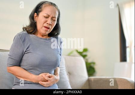 Malade et malade, femme asiatique âgée ayant des maux d'estomac, touchant son estomac avec une sensation douloureuse. Concept des problèmes de santé Banque D'Images