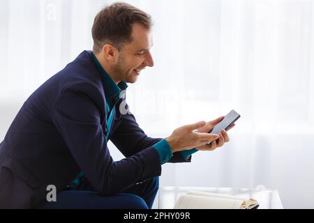 Homme d'affaires mûr souriant tenant un smartphone assis au bureau. pdg d'âge moyen utilisant des applications mobiles et un ordinateur portable pour téléphone portable. Technologie numérique Banque D'Images