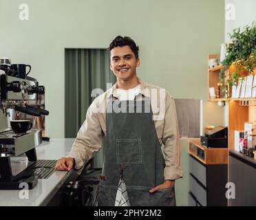 Un barista souriant dans un tablier regardant un appareil photo dans un café Banque D'Images
