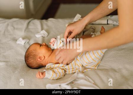 Maman robes mignon nouveau-né petit garçon dans une combinaison. Banque D'Images