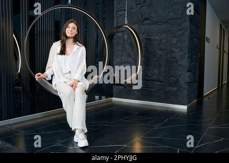 Jeune femme assise sur une chaise suspendue dans la clinique de beauté Banque D'Images