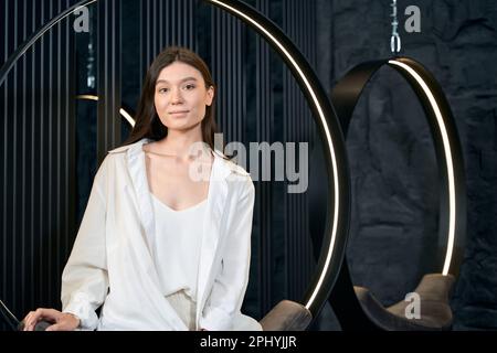 Femme assise sur une chaise suspendue dans la clinique de beauté Banque D'Images