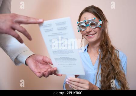 Souriante, la femme caucasienne est en train de lire le test dans le centre d'ophtalmologie Banque D'Images