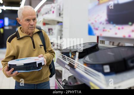 Sénior homme retraité achetant un aspirateur robotique dans la salle d'exposition du magasin d'appareils électriques Banque D'Images