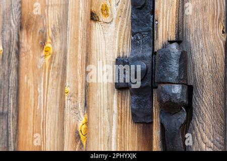 Anciens raccords de charnière noirs fabriqués par un forgeron. Raccords installés sur une ancienne porte en bois d'un ancien hangar Banque D'Images