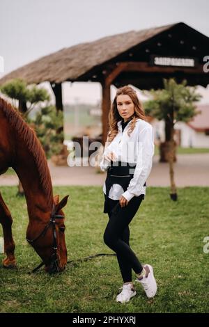 Une fille élégante avec des verres se tient à côté d'un cheval dans la rue. Banque D'Images