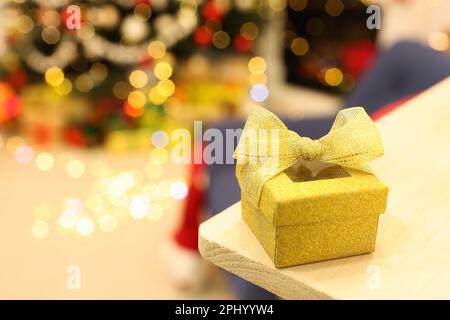 Boîte cadeau dorée sur étagère en bois contre les lumières de fête floues, espace pour le texte. Fête de Noël Banque D'Images