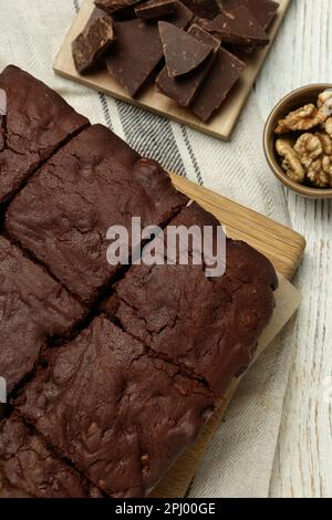 Délicieux brownies fraîchement cuits, noix et morceaux de chocolat sur une table en bois blanc, plat Banque D'Images