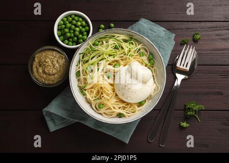 Bol de pâtes délicieuses avec burrata, petits pois et courgettes servi sur une table en bois, plat Banque D'Images