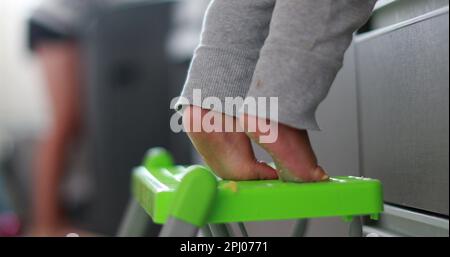 Un enfant sur une pointe debout sur une petite chaise à la cuisine. Bébé se tenir debout sur les orteils Banque D'Images