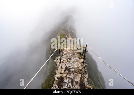 Randonneurs dans la brume, randonnée de Pico Arieiro à Pico Ruivo, sentier étroit exposé sur la falaise rocheuse, montagnes centrales de Madère, Madère, Portugal Banque D'Images