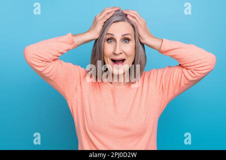 Portrait de drôle ecstatique surjoyeuse personne âgée avec bob Hairdo porter des bras de chemise roses sur la tête en regardant isolé sur fond bleu de couleur Banque D'Images