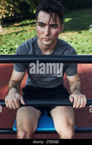 Portrait d'un jeune homme ayant une pause pendant son entraînement dans un parc d'entraînement moderne de rue calisthénique. Homme assis sur une planche assise portant des vêtements de sport l Banque D'Images