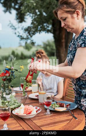 Femme ayant un repas du grill pendant l'été pique-nique familial dîner en plein air dans un jardin à la maison. Gros plan des personnes assises à une table avec de la nourriture et de la vaisselle Banque D'Images