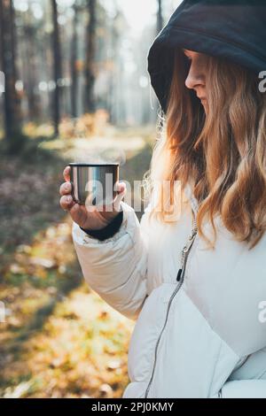 Femme dans une hotte ayant une pause pendant le voyage d'automne tenant une tasse avec une boisson chaude de thermos fiole le jour d'automne froid. Fille active errant dans une forêt ac Banque D'Images