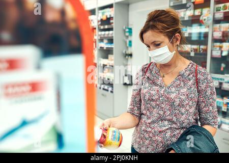 Une femme qui fait ses courses à la pharmacie, achète des médicaments, porte un masque facial pour couvrir la bouche et le nez pendant l'éclosion du coronavirus pandémique Banque D'Images