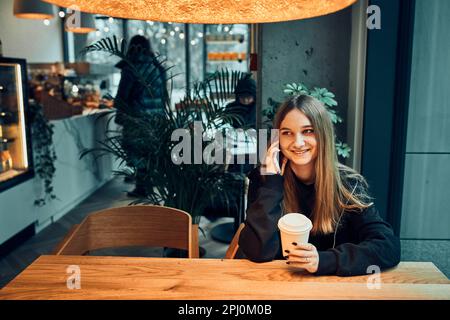 Jeune femme parlant au téléphone au café, ayant un appel agréable, répondant à l'appel, bavardant par téléphone mobile avec un ami tout en étant assis dans un café A. Banque D'Images