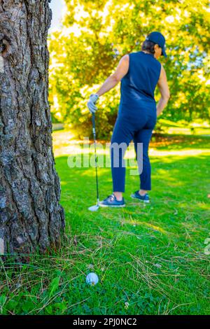 Balle de golf située sur l'herbe rugueuse et golfeur avec Golf Club à la recherche de la balle de golf dans les arbres en une journée ensoleillée en Suisse. Banque D'Images