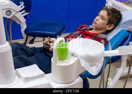 Jeune garçon sérieux dans la chaise dentaire dans la clinique. en attente de soins dentaires. Patient dans une chaise dentaire. Adolescent ayant un traitement dentaire chez le dentiste Banque D'Images