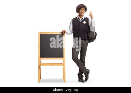 Portrait complet d'un étudiant afro-américain en uniforme, appuyé sur un tableau noir et faisant le geste des pouces, isolé sur fond blanc Banque D'Images