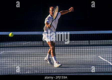 JOUEUR DE TENNIS MASCULIN ÂGÉ BACKHAND BALANÇOIRE AU-DESSUS DU FILET SUR UN COURT DE TENNIS EN TERRE BATTUE Banque D'Images