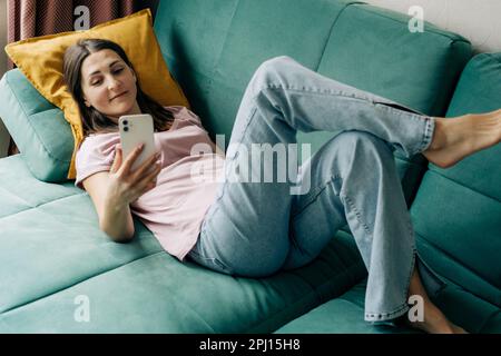 Une femme posée sur un canapé utilise un téléphone pour les appels vidéo. Banque D'Images