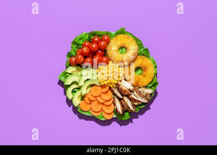 Vue ci-dessus avec salade de poulet hawaïen sur une assiette, isolée sur fond violet. Délicieux plat d'été, salade avec ananas rôti et poulet an Banque D'Images