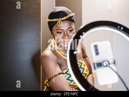 Une femme portant une robe africaine travaille sur des vidéos avec son téléphone portable Banque D'Images