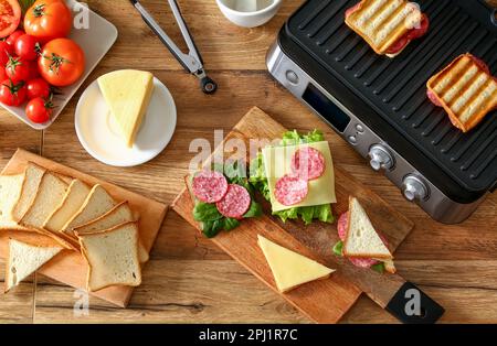 Composition avec grill électrique moderne et délicieux sandwiches sur table en bois Banque D'Images