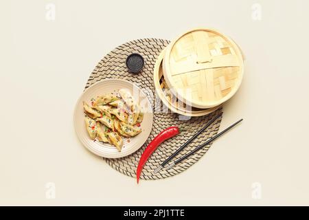Assiette avec savoureuse jiaozi chinoise, piment rouge et cuiseur vapeur en bambou sur fond blanc Banque D'Images