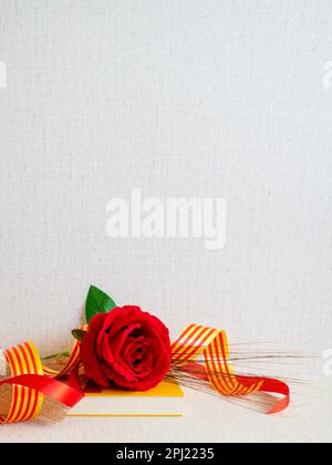 Sant jordi, rosa roja sobre libro amarillo con cintas con la bandera catalana y una cinta roja sobre fondo con textura Banque D'Images