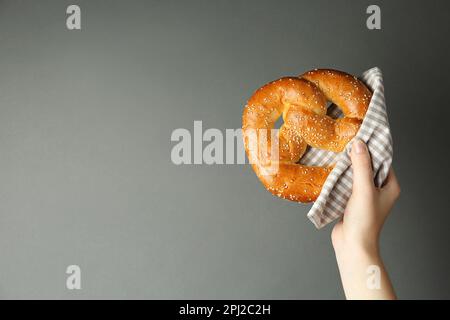 Femme avec de savoureux bretzel fraîchement cuit sur fond gris, gros plan. Espace pour le texte Banque D'Images