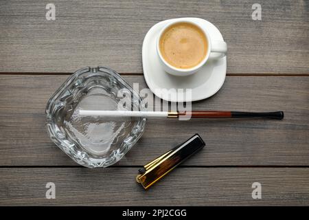 Cendrier avec porte-cigarettes long, briquet et tasse de café sur table en bois, plat Banque D'Images