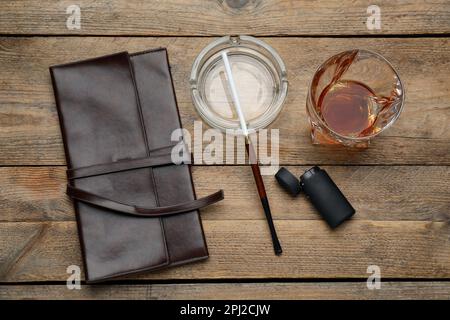 Cendrier en verre avec porte-cigarettes long, briquet, pochette et boisson alcoolisée sur table en bois, plat Banque D'Images